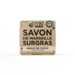 Un pain de savon carré étiqueté « Savon de Marseille Surgras » avec « Huile de Coco Corps & Mains » en dessous. L'emballage comporte également le logo "mkl green nature" et la mention "98% d'origine naturelle" et "Fabriqué en France. Dakar