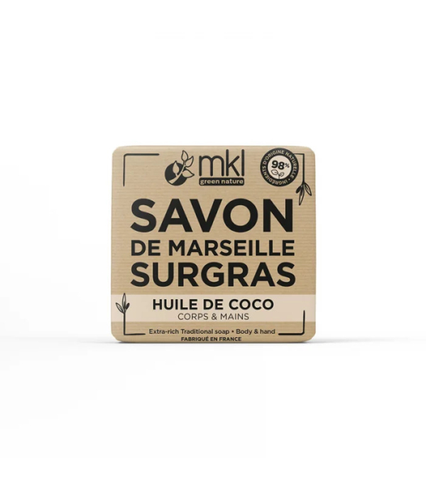 Un pain de savon carré étiqueté « Savon de Marseille Surgras » avec « Huile de Coco Corps & Mains » en dessous. L'emballage comporte également le logo "mkl green nature" et la mention "98% d'origine naturelle" et "Fabriqué en France. Dakar