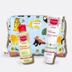 Un petit sac aux imprimés animaliers contient deux produits de maternité Mustela. Devant, un flacon d'huile vergetures, étiqueté « BIO », et un tube de crème vergetures. Le fond est blanc. Dakar