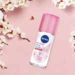 Un flacon de Sérum Blanchissant Profond Nivea au bouchon rose est posé sur un fond rose pastel entouré de fleurs de cerisier. L'étiquette indique des bienfaits comme une protection 48 heures et un parfum de sakura. Dakar