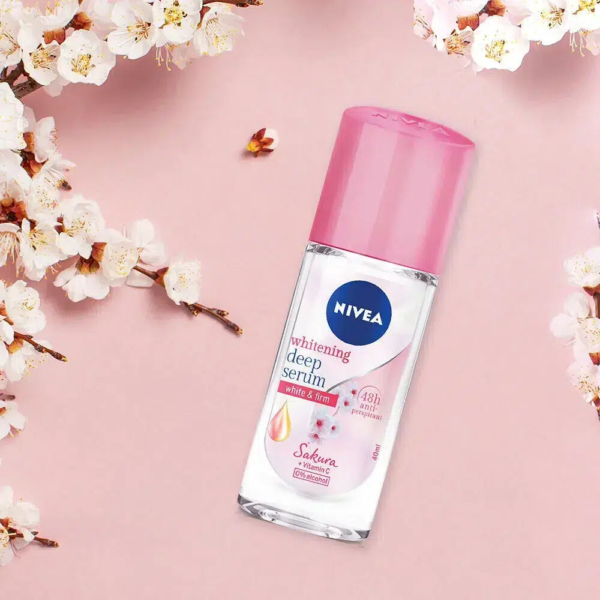 Un flacon de Sérum Blanchissant Profond Nivea au bouchon rose est posé sur un fond rose pastel entouré de fleurs de cerisier. L'étiquette indique des bienfaits comme une protection 48 heures et un parfum de sakura. Dakar