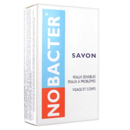 Boîte blanche étiquetée « Nobacter » en bleu et rouge, avec « SAVON » au-dessus. Le texte français suggère qu'il est destiné aux peaux sensibles et aux zones à problèmes du visage et du corps. Le Savon Nobacter 100 g est idéal pour obtenir un teint éclatant sans effort. Dakar