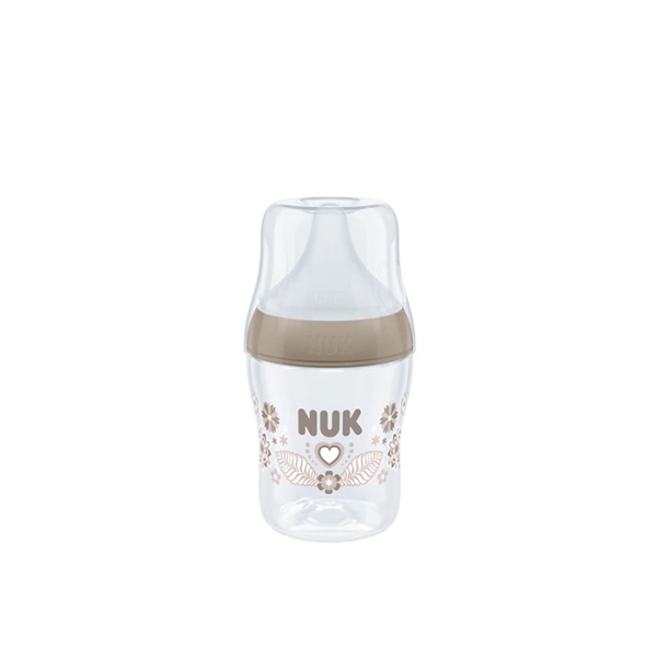 Biberon transparent au design beige, orné du mot « NUK » imprimé au centre, orné de motifs floraux et d'un cœur. Doté d'un grand bouchon et d'une base large, il se détache sur un fond blanc uni. Dakar