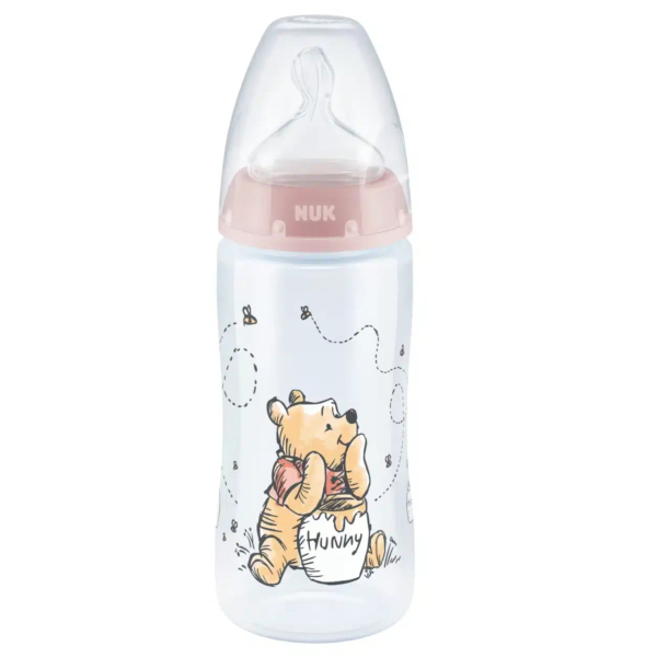 Un biberon avec un bouchon et une tétine roses, représentant un ours de dessin animé, rappelant Winnie l'ourson, tenant un pot de miel étiqueté « Miel ». Des abeilles voltigent autour de l'ourson sur le biberon. Dakar