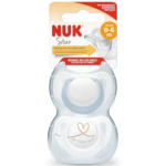 Image d'une sucette NUK Star en silicone pour les bébés de 0 à 6 mois. L'emballage est blanc avec des touches orange et jaune, orné d'un cœur et de l'inscription « Ma première NUK ». La sucette est transparente et de forme symétrique. Dakar