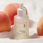 Un flacon compte-gouttes givré étiqueté « numbuz:n Serum 3, BODLEBODLE REPAIR » est placé parmi des pêches sur un fond en tissu blanc, créant une esthétique fraîche et minimaliste. Dakar