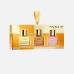 Coffret de trois huiles Nuxe Huile Prodigieuse dans un coffret cadeau doré avec anse en ruban. Les huiles sont présentées dans des flacons transparents aux teintes variées : jaune, bronze et rose. L'emballage est orné du logo Nuxe. Dakar