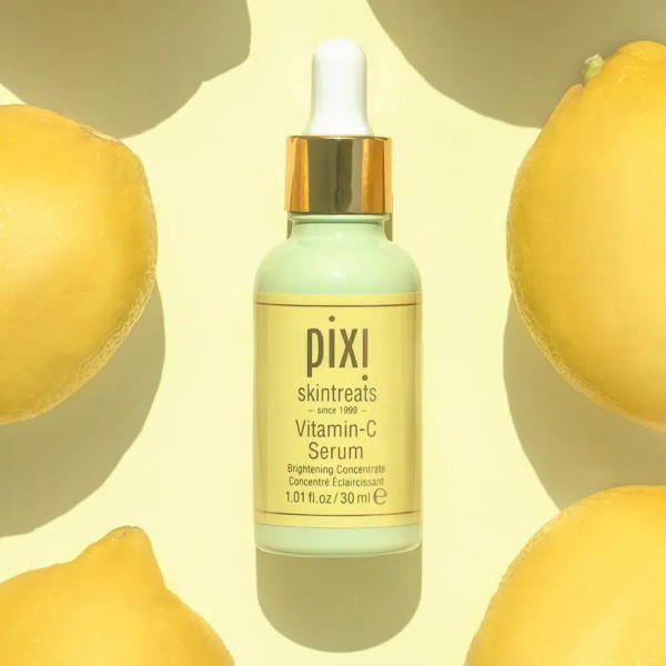 Un flacon compte-gouttes de sérum à la vitamine C Pixi est centré sur un fond jaune clair, entouré de citrons entiers. L'étiquette du flacon le décrit comme un concentré éclaircissant. Dakar