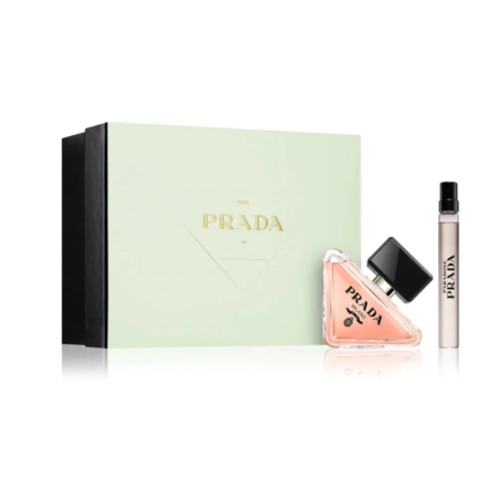 Un coffret de parfums Prada comprenant une boîte vert clair avec des lettres dorées, un flacon de parfum rose triangulaire avec un bouchon noir et un petit flacon pulvérisateur de voyage. Dakar