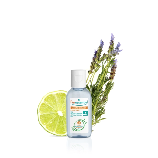 Un flacon de Gel Désinfectant Puressentiel pour les Mains est présenté sur un fond blanc. Derrière lui se trouvent un demi-citron vert et des brins de lavande et de romarin, suggérant des ingrédients naturels. Dakar