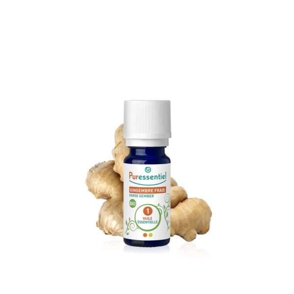Un petit flacon bleu d'huile essentielle de gingembre frais Puressentiel, coiffé d'un bouchon blanc, est posé devant des morceaux de racine de gingembre frais. L'étiquette présente un texte vert et orange, rehaussé de touches décoratives. La racine de gingembre est brun clair et bosselée. Dakar