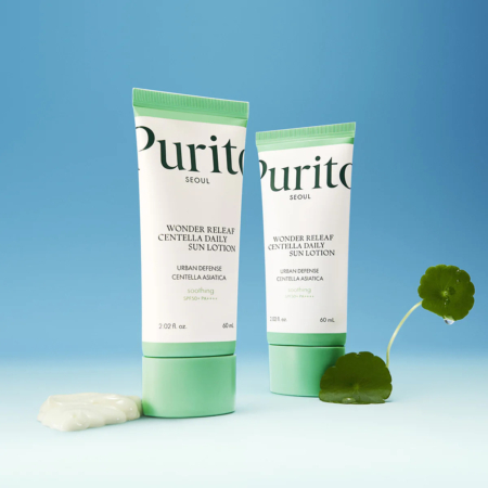 Deux tubes de lotion solaire quotidienne Purito Seoul Wonder Relief Centella sont présentés sur un fond bleu. L'un est droit, l'autre légèrement incliné. Une petite noisette de lotion et une feuille de Centella sont placées à côté. Dakar