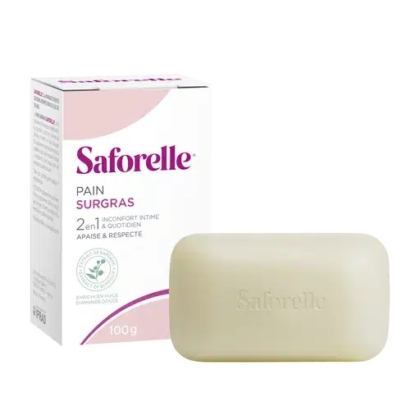 Une boîte et un pain de savon Saforelle Pain Surgras. L'emballage, majoritairement blanc avec un texte violet, souligne le caractère 2-en-1 de ce produit, pour un usage intime et quotidien, pesant 100 g. Le pain de savon est beige clair et rectangulaire. Dakar