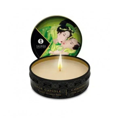 Une bougie de massage ronde, étiquetée « Shunga », présentée dans un contenant noir au parfum de thé vert. Le couvercle, orné d'un couple en tenue traditionnelle, s'ouvre derrière la bougie allumée. Dakar