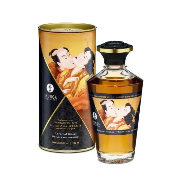 Un flacon d'huile chauffante Shunga Erotic Art est présenté à côté de son emballage cylindrique. Tous deux sont ornés d'une illustration traditionnelle japonaise représentant un couple enlacé. L'étiquette porte l'inscription « Baisers Caramel » et l'huile est de couleur ambrée. Dakar