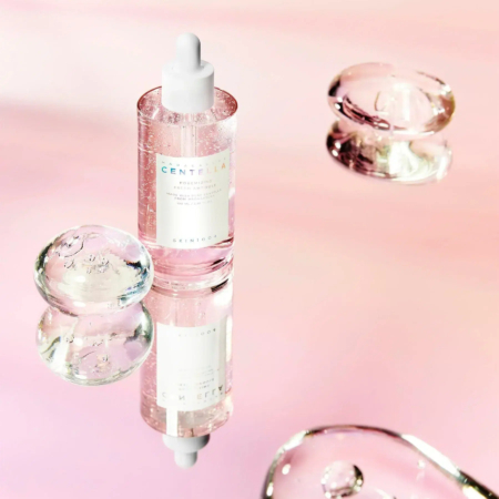 Un flacon compte-gouttes de sérum de soin, étiqueté « Centella », est posé sur une surface réfléchissante, entouré de sphères transparentes semblables à du gel. Le fond est un doux dégradé de teintes roses, créant une esthétique sereine et élégante. Dakar