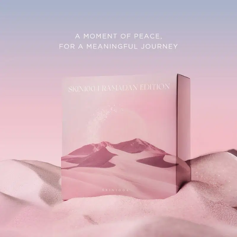 Une boîte rose étiquetée "SKIN1004 RAMADAN EDITION" repose sur du sable rose doux avec des montagnes pastel derrière. Au-dessus, le texte se lit comme suit : "UN MOMENT DE PAIX, POUR UN VOYAGE PLEIN DE SENS". Avec Skin1004 Coffret Illuminateur Anti Taches et Hydratant Édition Limitée 3 Pièces. Dakar