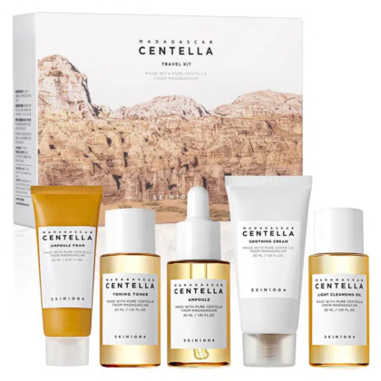 Un coffret de voyage de soins de la peau comprenant cinq produits dans un emballage blanc et ambré. Il comprend une mousse ampoule, une lotion tonique, une ampoule, une crème apaisante et une huile nettoyante. L'arrière-plan présente un paysage rocheux intitulé « Centella de Madagascar ». Dakar