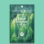 Un sachet vert étiqueté « Spot Cover Patch » avec une image de forêt dense. Ce sachet contient 22 patchs et est de la marque SKIN1004. Le fond est bleu sarcelle uni. Dakar