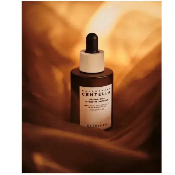 Un flacon compte-gouttes étiqueté « Centella » et portant l'inscription « SKIN1004 » au fond est entouré d'un tissu fluide et doré. L'ensemble crée une ambiance chaleureuse et luxueuse. Dakar