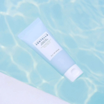 Un tube de produit de soin bleu clair étiqueté « Skin1004 » et « Centella » flotte sur une eau claire et bleu pâle, projetant une ombre douce. Dakar