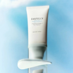 Un tube de sérum en feuille à la centella de Madagascar de SKIN1004 est positionné sur un fond bleu et blanc doux. Le tube est vertical et les informations sur le produit sont imprimées en noir. En dessous, une trace de sérum est visible sur une surface transparente. Dakar