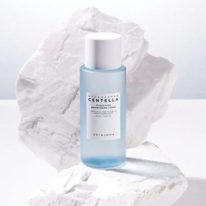 Un flacon bleu de tonique éclaircissant SKIN1004 Madagascar Centella Hyalu-Cica est posé sur un fond blanc texturé, évoquant des rochers. L'étiquette du flacon est visible, avec les détails du produit et la marque. Dakar
