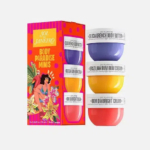 Un coffret coloré de mini-savons Sol de Janeiro Body Paradise, composé de quatre petits contenants empilés verticalement : beurre corporel Delicia Drench, crème Brazilian Bum Bum, crème éclat Bum Dia et Bom Dia. Emballage lumineux au design tropical. Dakar