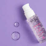 Un flacon pompe transparent de crème hydratante SVR Aqua Sensifine est posé sur un fond violet. Deux gouttes de produit sont disposées à côté du flacon, ajoutant un éclat réfléchissant à la scène. Dakar