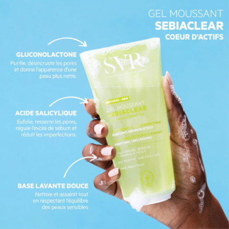 Une main tenant un tube de gel nettoyant moussant SVR Sebiaclear sur fond bleu. L'emballage met en valeur des ingrédients tels que la gluconolactone, l'acide salicylique et une base nettoyante douce, soulignant ses propriétés purifiantes et désincrustantes. Dakar