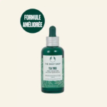 Un flacon vert de la Solution Quotidienne à l'Arbre à Thé de The Body Shop, muni d'un bouchon compte-gouttes, est présenté sur un fond clair. Le texte sur le flacon mentionne l'acide salicylique et son adéquation aux peaux à imperfections. Un cercle vert indique « FORMULE AMÉLIORÉE ». Dakar