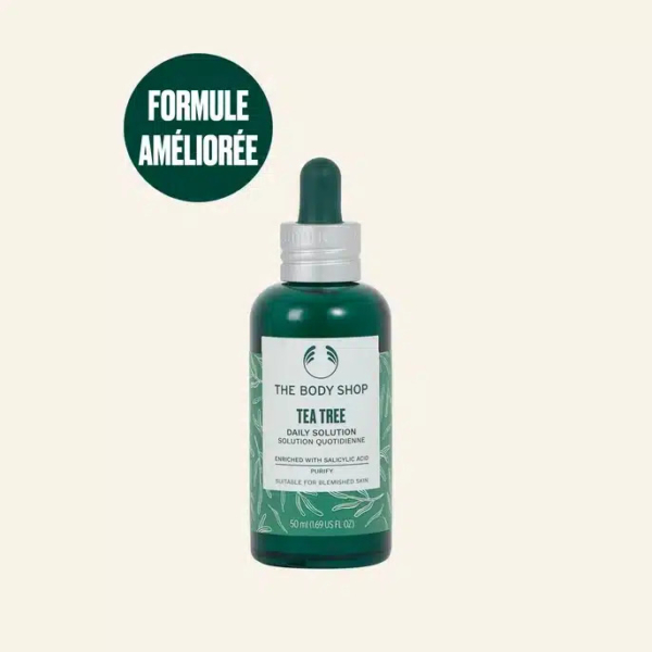 Un flacon vert de la Solution Quotidienne à l'Arbre à Thé de The Body Shop, muni d'un bouchon compte-gouttes, est présenté sur un fond clair. Le texte sur le flacon mentionne l'acide salicylique et son adéquation aux peaux à imperfections. Un cercle vert indique « FORMULE AMÉLIORÉE ». Dakar