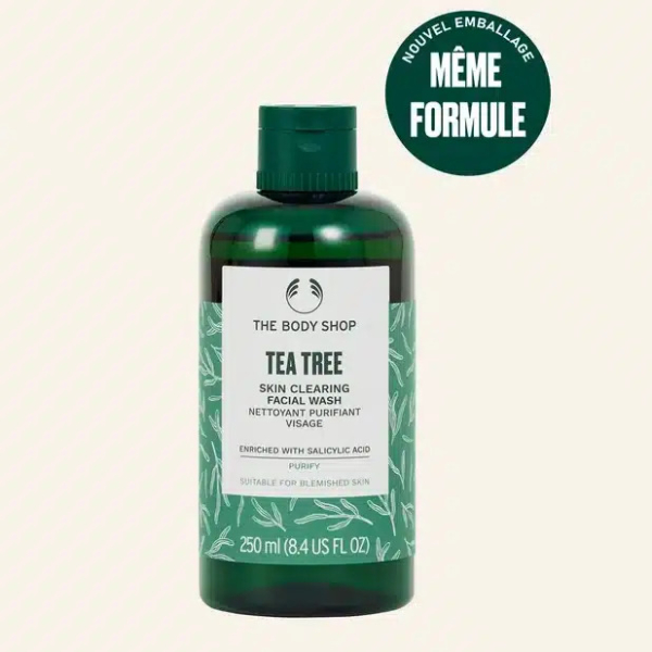 Un flacon vert de nettoyant visage purifiant à l'arbre à thé The Body Shop, avec un bouchon vert. L'étiquette indique « Enrichi en acide salicylique » et convient aux peaux à imperfections. Un graphisme circulaire indique « Nouvel emballage, même formule » en français. Dakar