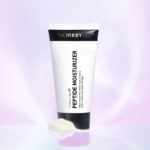 Un tube blanc de crème hydratante aux peptides The Inkey List se dresse sur un fond pastel doux. Une partie de la crème est pressée à la base du tube. Dakar