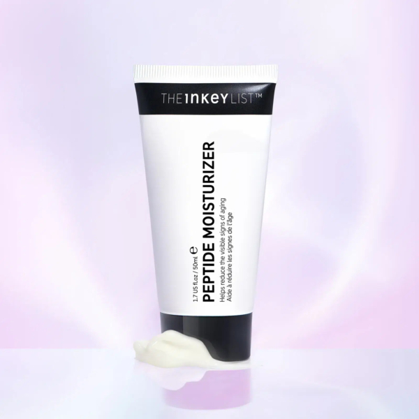 Un tube blanc de crème hydratante aux peptides The Inkey List se dresse sur un fond pastel doux. Une partie de la crème est pressée à la base du tube. Dakar