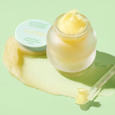 Un pot givré de Masque à Lèvres Exfoliant au Sucre et Citron Tocobo 20 ml, au design inspiré de LANEIGE, révèle une texture jaune crémeuse. Avec ses ingrédients à base de citron et d'huile d'olive, une touche de crème décore élégamment le fond vert pastel. Dakar
