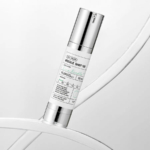 Une bouteille cylindrique de « REEDLE SHOT » de Needly, étiquetée comme contenant 50 ml et contenant du thé vert. La bouteille est métallique, avec des touches de blanc et de vert menthe, et se détache sur un fond clair et abstrait. Dakar