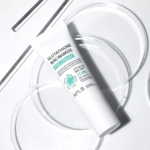 Un tube blanc de Aplb Glutathione Niacinamide Crème Éclat Contour Yeux Anti Poches 20 ml repose sur une surface blanche avec des disques circulaires transparents, brillamment éclairés. Dakar
