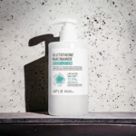Un flacon blanc de lotion corporelle au glutathion et à la niacinamide, muni d'une pompe, se détache sur un fond gris moucheté. L'étiquette détaille les ingrédients et la concentration de la lotion, avec notamment les mentions « LIPPO Gluta » et « 12,5 % ». Dakar