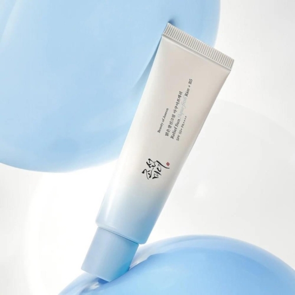Un tube blanc et bleu clair de Beauty of Joseon Relief Sun Aqua Fresh Rice + B5 Fluide Solaire SPF50 au panthénol 50 ml avec un texte coréen est posé en diagonale sur un fond bleu et blanc doux, accentué par des formes rondes bleu clair. Dakar