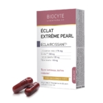 Une boîte de produit étiquetée « Biocyte Laboratoire Éclat Extrême Pearl » avec la description des ingrédients, notamment du L-Glutathion, du SkinAx², de la tomate blanche et du mûrier blanc. Deux capsules rouges sont placées devant la boîte. Dakar