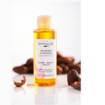 Un flacon d'huile de soin BYPHASE SUBLIMATRICE ARGAN 100 ml est présenté avec une étiquette transparente, entourée de noix d'argan concassées et d'une touche d'huile de sésame bio Waam. L'emballage transparent dévoile l'huile dorée à l'intérieur sur une surface blanche. Dakar