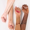 Trois bras aux carnations différentes portent des échantillons de fond de teint. Les échantillons sont numérotés de 10 à 400. Les ongles sont de couleurs variées : rose clair, rouge et nude. L'image présente une palette variée de nuances de maquillage. Dakar