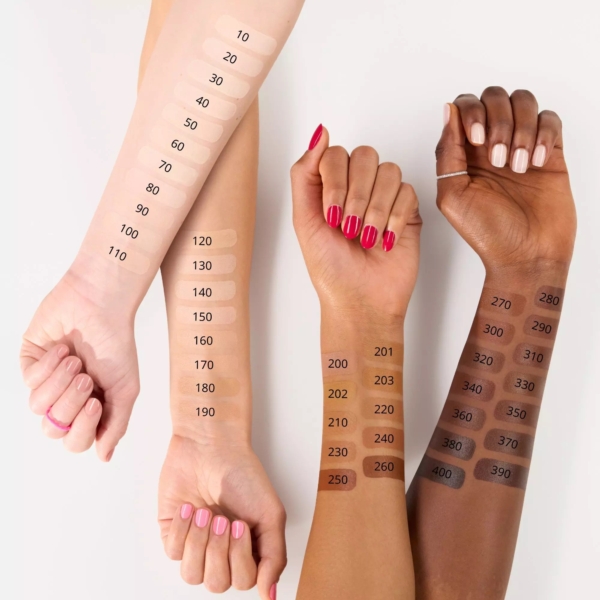 Trois bras aux carnations différentes portent des échantillons de fond de teint. Les échantillons sont numérotés de 10 à 400. Les ongles sont de couleurs variées : rose clair, rouge et nude. L'image présente une palette variée de nuances de maquillage. Dakar