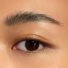 Un gros plan montre l'œil d'une personne avec un sourcil soigné, obtenu avec le Gel Fixation Sourcils Transparent Essence Fix It Like A Pro 8,5 ml. La peau paraît lisse et uniformément tonifiée, sublimée par un éclairage qui met en valeur l'éclat naturel de l'iris brun foncé. Dakar