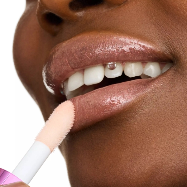Gros plan d'une personne appliquant du gloss rose sur ses lèvres à l'aide d'un applicateur. Les lèvres sont légèrement entrouvertes, révélant les dents, et la peau est lisse et éclatante. Le gloss apporte un fini brillant. Dakar