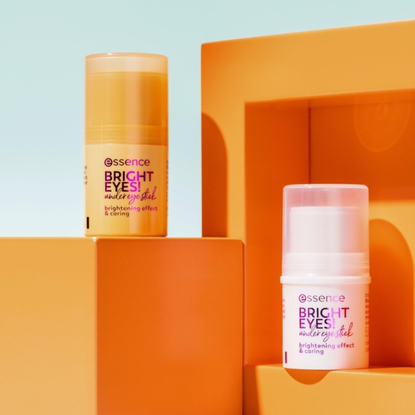 Deux sticks contour yeux anti-cernes Essence BRIGHT EYES, l'un orange et l'autre blanc, étiquetés « Effet éclaircissant et soin », reposent sur des blocs géométriques orange. Le fond vif, orné de formes et d'ombres, souligne l'élégance de ces essentiels pour le contour des yeux. Dakar