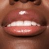 Gros plan sur les lèvres ornées d'Essence The SUPER BALM Glossy Baume à Lèvres Hydratant Rose Clair, légèrement entrouvertes pour révéler des dents blanches. Dakar