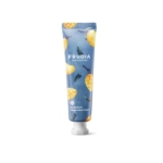 Un tube de Frudia Crème Mains Mon Verger à la Mangue 30 g se dresse sur un fond bleu, décoré de mangues et de feuilles. Le bouchon est blanc. Dakar