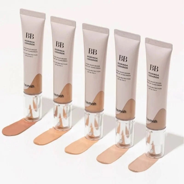 Cinq tubes de BB crème, étiquetés « Moringa Ceramide », sont alignés. Chaque tube distribue une teinte différente sur une surface blanche, présentant un dégradé de tons clairs à foncés. Les tubes portent la marque « Heimish ». Dakar